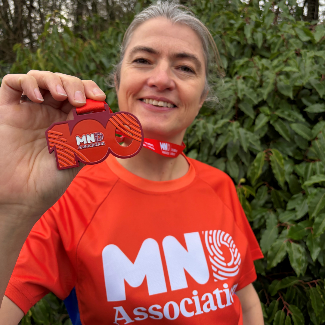 woman holding a terracotta medal in the shape of 100 and smilling